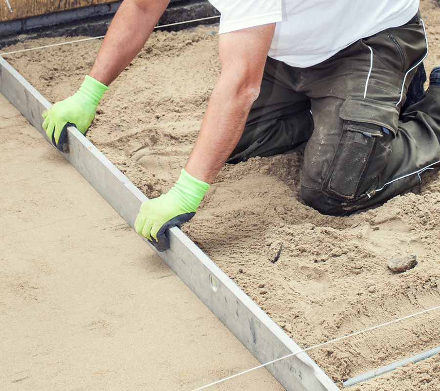 Bauarbeiter, der auf der Baustelle Bausand glättet.
