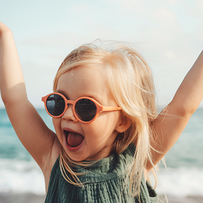 Hurra! Das Ferienhaus ist optimal versichert mit dem GEV Ferienhauskonzept Kleines Mädchen am Meer mit Sonnenbrille reißt jubelnd die Arme hoch. Wahrscheinlich freut sie sich über den innovativen Rundumschutz, den unsere Ferienhausversicherung bietet.