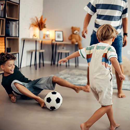 Darum ist eine Privathaftpflichtversicherung ist wichtig. Zwei Kinder spielen mit einem Erwachsenen Fußball in der Wohnung.