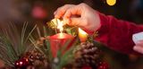 Ein Mädchen zündet eine Kerze eines Adventsgesteckes an. Schön, aber brandgefährlich. Vorsicht ist geboten.