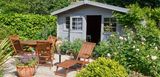 Gartenhaus inmitten eines üppig begrünten Gartens mit Gartenmöbeln, Gartengeräten und mehreren Pflanztöpfen mit Blumen und anderen Pflanzen