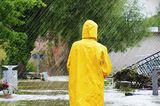 Frau mit gelben Regenmantel und Gummistiefeln steht im Starkregen 