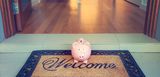 Sparschein steht auf Fußmatte mit Aufdruck "welcome", die Wohnungstür dahinter ist offen. Nur wenn man das Sparschwein mit der Kaution füttert, darf man in die Wohnung. 