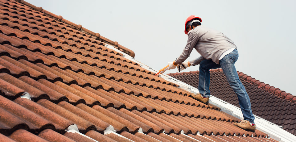 Dachwartung: Ein Mann mit Bauhelm dichtet Stellen an einem Dach ab
