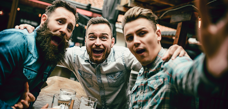 Drei junge Männer beim ausgelassenen Feiern mit Bier – typische Szene am Vatertag