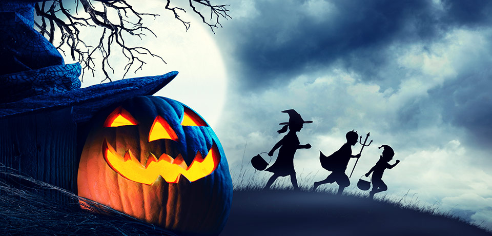 Ein gruseliges Halloweenbild: Vorne ein Kürbis, dahinter der fahle Mond und verkleidete Hexen und Gespenster im Mondlicht, die einen Hügel herablaufen...