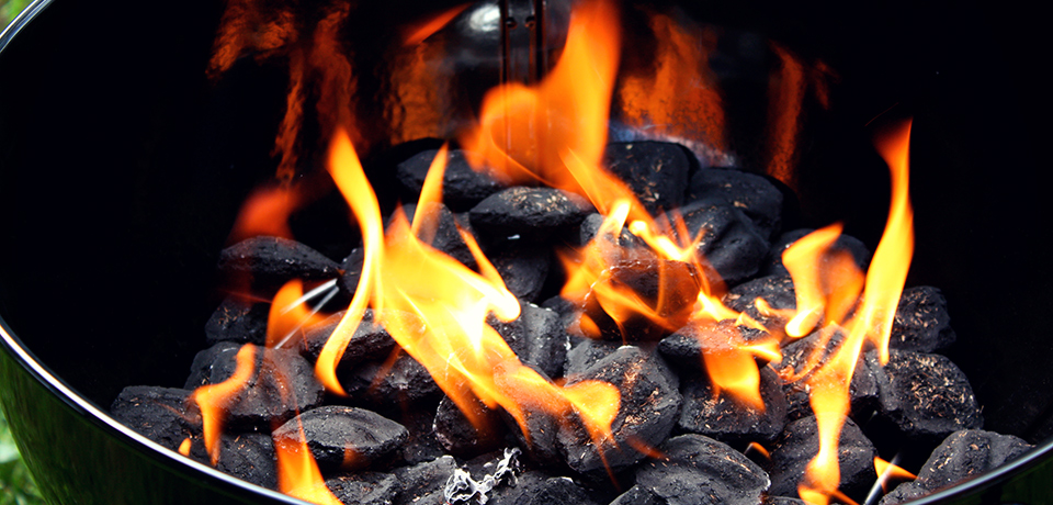 Sicher grillen mit Holzkohle: Hausrat und Wohngebäude absichern Brennende rundliche Holzkohlebriketts in einem schwarzen Grill, noch nicht durchgeglüht