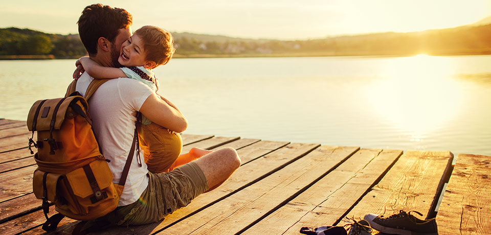 Vater und Sohn sitzen auf einem Steg an einem See im Sonnenuntergang. Die Privathaftpflicht der GEV bietet ihren Versicherten sorglose Sicherheit.