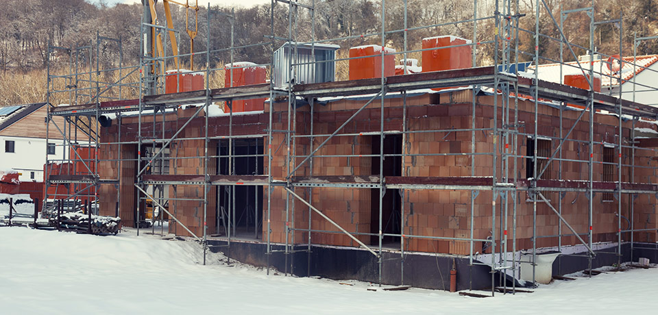 Baustelle im Schnee. Die Bauarbeiten ruhen aufgrund des Wetters. Die Bauleistungsversicherung übernimmt die Kosten für Bauverzögerungen, wenn der Schnee zu unüblicher Zeit fällt. 