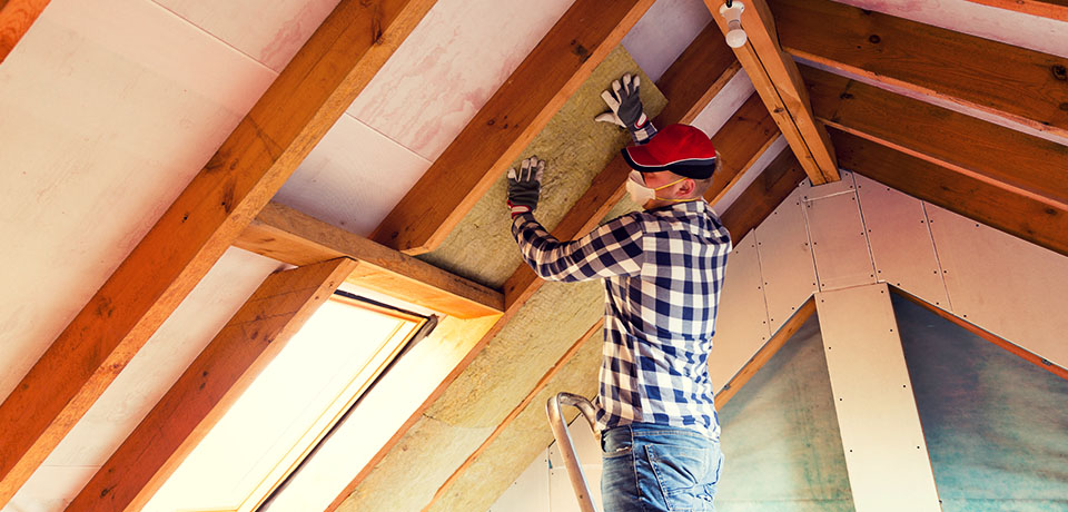 Handwerker verlegt Klemmfilz für die Dämmung des Daches. Der Fachbegriff für diese Dachdämmung lautet: Zwischensparrendämmung