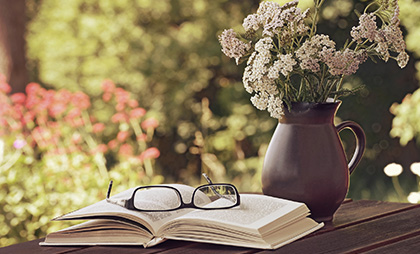 Auf dem Tisch eine Blumenvase mit bienenfreundlicher Schafgarbe, daneben Buch und Lesebrille.