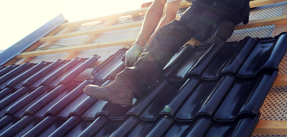 Ein Dachdecker sitzt auf dem Dach und legt Dachziegel. Eine Dachsanierung sollte von fachkundigen Handwerkern durchgeführt werden. 
