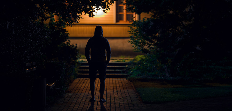 Ein Mann beobachtet aus dem Dunkeln heraus ein Haus. Ein Einbrecher?