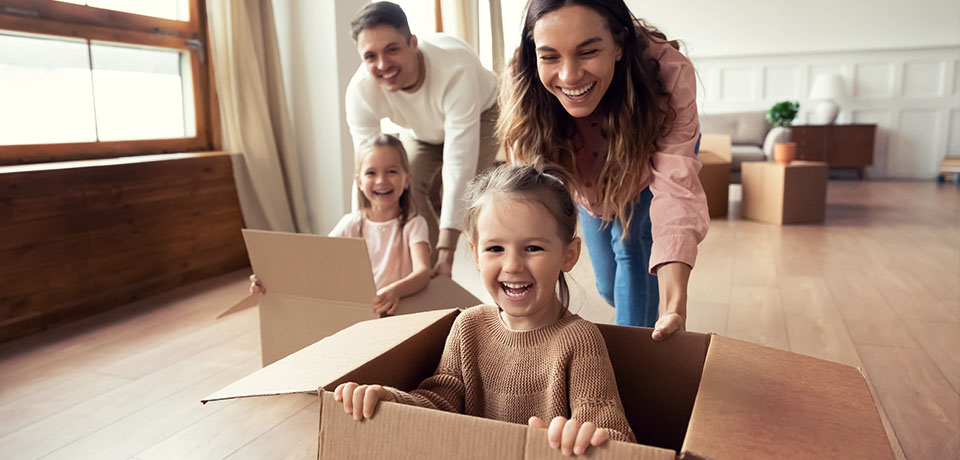 Kinder in Umzugskartons werden von den Eltern um die Wette geschoben. Nach dem Umzug ins neue Haus gibt es nur zwei Optionen: Die Wohngebäudeversicherung wurde vom Vormieter übernommen oder es wurde eine neue Wohngebäudeversicherung abgeschlossen.  