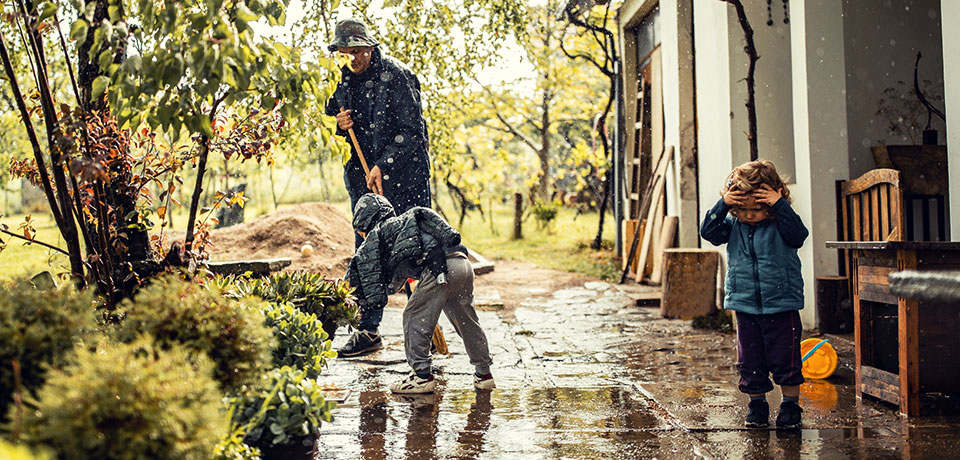 Vater schippt mit seinen Kindern das Regenwasser aus dem Hof des Hauses. 
