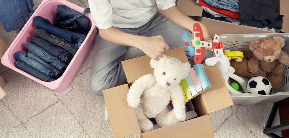 Ein Junge sortiert aus: Er teilt Kleidung und Spielsachen auf in Behalten- und Verschenken-Kisten.